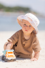 Wall Mural - toddler boy plays on a sandy beach in a panama hat and cotton clothes in summer