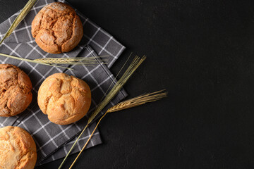 Canvas Print - Napkin with delicious buns and wheat ears on black background