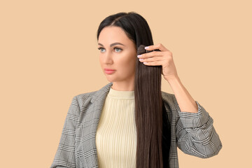 Wall Mural - Female hairdresser with strand of brunette hair on beige background, closeup