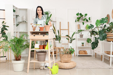 Wall Mural - Beautiful young woman with gardening tools taking care of houseplant at home