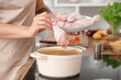 © Pixel-Shot - Young housewife with chicken drumsticks cooking soup on stove in kitchen, closeup