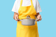 © Pixel-Shot - Young woman in apron holding cooking pot with tasty soup on blue background, closeup