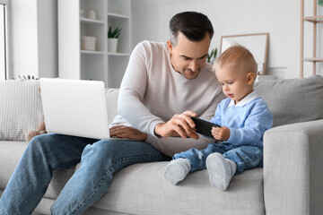 Wall Mural - Father working while his little child playing with mobile phone at home