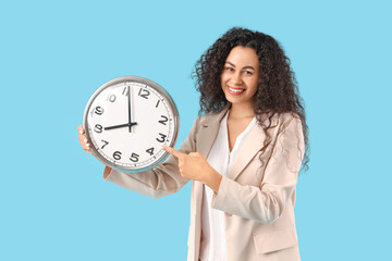 Wall Mural - Young African-American businesswoman with clock on blue background. Time management concept