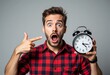 © DesignDividends - Man in red plaid shirt holding black alarm clock pointing finger