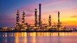 © jiraphat - A large industrial plant is lit up at sunset. The sky is a mix of orange and pink hues
