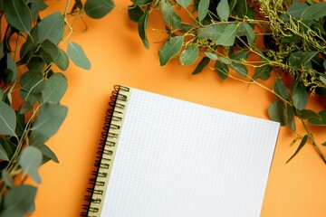 Poster - A notepad with a pen and a small plant on an orange surface, great for creative ideas or office inspiration