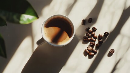 Poster - Top view of a creamy brown coffee cup surrounded by roasted coffee beans on a light surface with soft sunlight and green leaves shadowing the scene