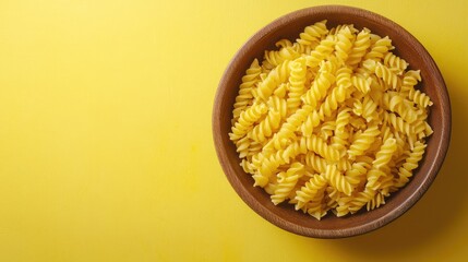 Leinwandbilder - Aromatic Fusilli Pasta in a Brown Bowl on Bright Yellow Background Featuring Space for Text and Culinary Inspiration