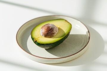 Poster - A halved avocado with a visible pit rests on a speckled plate, bathed in sunlight.