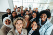 © Jacob Lund - Multiethnic corporate team taking a group selfie together inside an office building