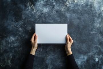 Poster - Overhead view of hands holding a blank white paper sheet on a dark textured background.