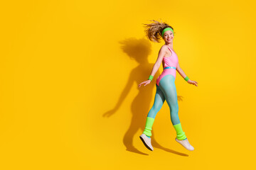 Wall Mural - Young woman in retro aerobics outfit jumping joyfully against vibrant yellow background, showcasing fitness and healthy lifestyle