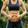 © KenPix - Athletic female torso, toned abs, hands forming heart shape over stomach, dark sports bra, outdoor setting, soft natural lighting, fitness motivation, body positivity, self-love concept, blurred green