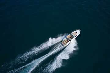 Wall Mural - Luxury white speedboat cruising on turquoise water, creating a splash under the summer sun. Aerial top view with sun reflection, perfect for travel, holidays, and nautical themes.