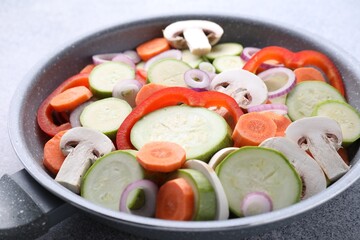 Wall Mural - Frying pan with mix of fresh vegetables and mushrooms on grey table, closeup