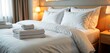 © miss irine - Luxurious hotel room bed with fresh white linens. Clean white sheets, duvet cover neatly arranged. Folded towels placed on top. Room warm lighting. Hotel bedding neatly made ready for guest. Hotel