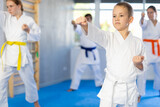 Boy dressed in white kimono with belt practice punches techniques with trainer, in background his family is doing kata