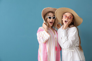 Wall Mural - Young sisters in summer hats and sunglasses on blue background