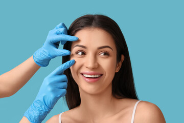 Wall Mural - Beautician touching face of young woman on blue background