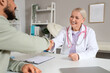 © Pixel-Shot - Female doctor with young man shaking hands at table in clinic