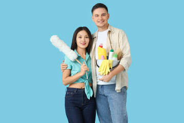 Poster - Cute young couple with cleaning supplies and pp-duster on blue background