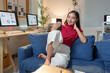 © Phimwilai - Young asian businesswoman working from home, having a video call with a client on smartphone while sitting on sofa in living room at night with computer showing charts and graphs on the desk