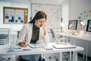 Poster - Young professional woman suffering from headache while analyzing financial charts at her desk in a modern office