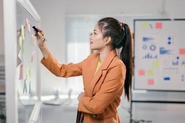 Wall Mural - Businesswoman using colorful sticky notes while brainstorming and strategizing on a transparent whiteboard in a modern office