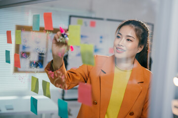 Poster - Professional woman writing notes on glass board during collaborative team strategy session