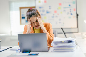Poster - Young asian businesswoman suffering from headache while working on laptop in office with documents on desk