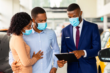 Wall Mural - Salesperson In Medical Mask Consulting Black Spouses In Dealership Center, African American Couple Choosing New Vehicle In Modern Automobile Showroom During Coronavirus Pandemic, Closeup