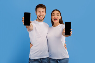 Poster - We Like This. Laughing girl and guy showing their smart phones with black blank screen to camera, purple wall, mock up