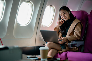 Aufkleber - Businesswoman using laptop and wearing wireless earphones while traveling by airplane