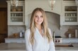 © Aleksander - A young woman with long blonde hair smiles warmly in a bright Modern Farmhouse interior design style kitchen. She wears a white blouse and stands confidently in front of a marble countertop.