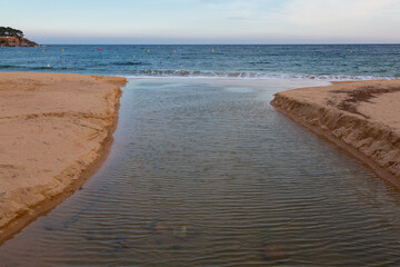 Stream flowing into the sea between sandy banks on a cloudy day