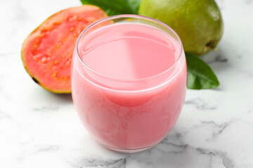 Wall Mural - Tasty guava juice in glass, leaves and fruits on white marble table, closeup