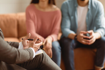 Help Concept. Closeup Cropped View Of Man Counselor Therapist Or Consultant In Suit Talking With Couple Sitting In Office, Giving Professional Advice. Selective Focus On Hands With Clipboard And Pen