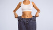 © Prostock-studio - Closeup cropped view of skinny woman showing flat stomach pulling oversized big blue pants jeans. Slim body low fat. Healthy size athletic posing girl isolated over blue color studio background