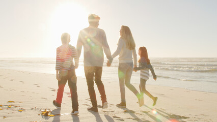 Wall Mural - Rear View Of Family Walking On Winter Beach Holding Hands With Flaring Sun