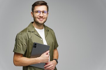 Young man smiling while holding a tablet and wearing stylish glasses in a studio setting