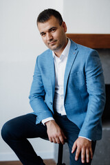 Wall Mural - portrait of a young groom in a blue jacket and white shirt in a bright studio