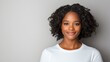 © Tondone - A young woman with curly hair smiling confidently. She is wearing a white shirt against a neutral background, radiating positivity and self-assurance.
