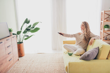 Wall Mural - Charming young woman enjoying a relaxed weekend at home in a cozy living room, dressed in casual stripes, daylight streaming in