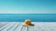 © Olena - A simple summer concept with a single straw hat resting on a sun-bleached wooden deck, with the bright blue sky and the ocean in the background.
