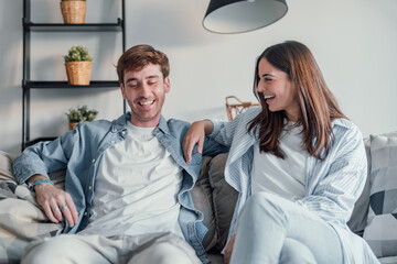 Young happy couple having fun talking laughing relaxing at home on couch, boyfriend embracing girlfriend telling funny joke sitting on sofa, humor in relationships, enjoying weekend together.