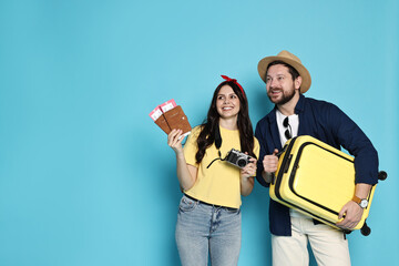 Wall Mural - Tourism. Happy couple with passports, tickets and suitcase on light blue background, space for text