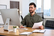 © New Africa - Man with document working on computer at table in office