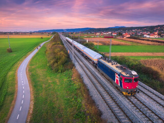 Wall Mural - aerial view of freight train moving near alpine village, mountains and green fields, bike path at su