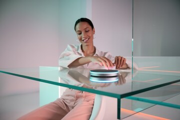 Poster - Woman interacts with a futuristic, illuminated smart device on a glass table.
